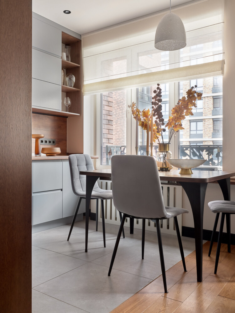Столовая зона состоит из прямоугольного стола на длинных темных ножках и стульев в тон фасадам кухонного гарнитура.